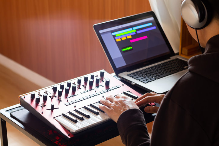 A student producing music with a keyboard, controller, and laptop