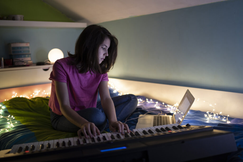 A young girl learning a new song from her laptop for digital piano sitting on her bed