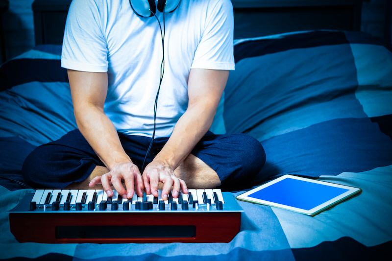 man learning online music lesson and playing keyboard on bed in bedroom at night